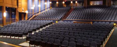 The seating of the westbrook performing arts center from the stage. Seats are navy blue and you can see floor lights along each section and on the stairs in the upper section.